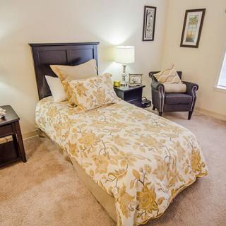A cozy bedroom with a single bed, nightstand, and armchair adorned with elegant decor.