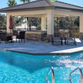A luxurious outdoor pool area with lounge chairs and patio furniture under a shaded pavilion.