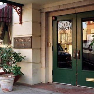 The entrance to a building with green double doors and a potted plant beside them.