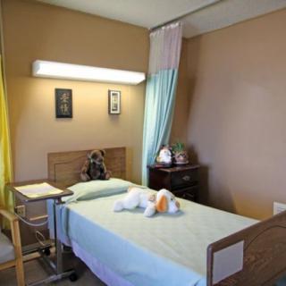 A hospital room with a single bed, teddy bear, and medical equipment.