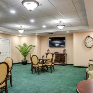 A well-lit conference room with a central table and chairs, featuring a television, decorative plant, and wall clock.