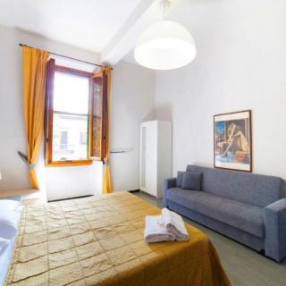 A bright and cozy bedroom with a bed, sofa, wardrobe, and a large window with yellow curtains.