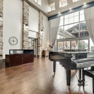 A modern living room with a grand piano, featuring large windows and high ceilings.