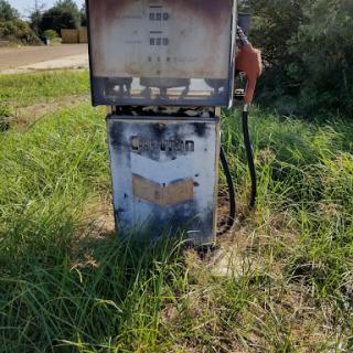 An old, abandoned fuel pump surrounded by overgrown grass.