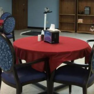 A dining area with a round table covered in a red tablecloth, surrounded by chairs.
