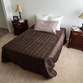 A neatly made bed with a decorative brown coverlet, situated in a cozy room.