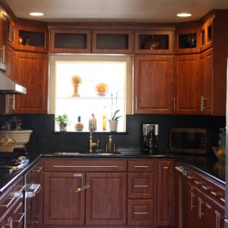 A modern kitchen with wooden cabinets and dark countertops, featuring a window above the sink.