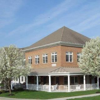 A brick building with a porch surrounded by blooming trees under a blue sky.