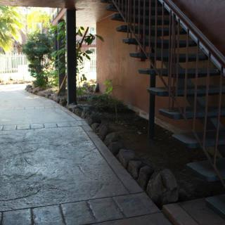 A shaded outdoor walkway featuring a spiral staircase and lush plants along the path.