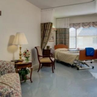 A well-lit hospital room with a bed, chair, lamp, and sofa.
