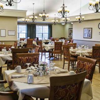 An elegant dining room setup with neatly arranged tables and chairs, featuring ornate chandeliers.