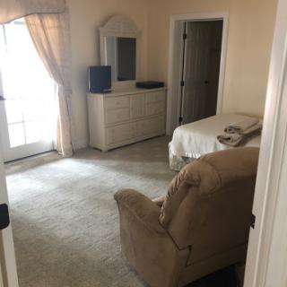 A cozy and simple bedroom setup with a dresser, television, and comfortable seating.