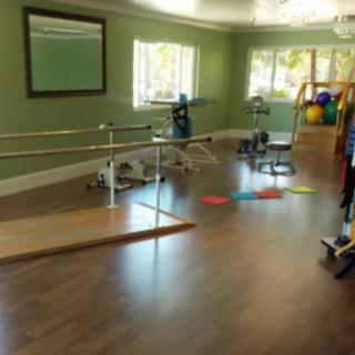 A well-equipped physical therapy room with rehabilitation equipment and a mirrored wall.