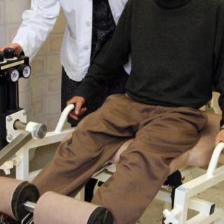 A patient undergoing physical therapy with the assistance of a therapist using exercise equipment.
