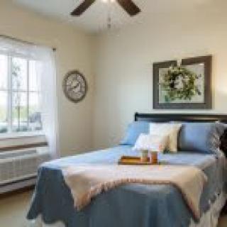 A cozy bedroom with a neatly made bed, wall clock, and decorative wreath on the wall.