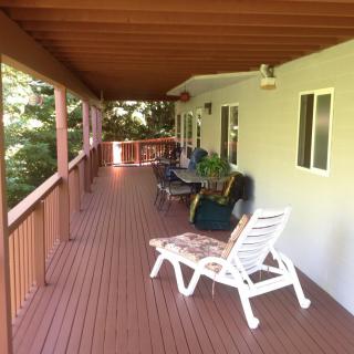 A spacious wooden deck with lounge chairs and a table, sheltered by an overhanging roof.