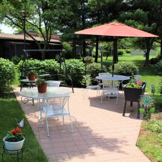 A sunny garden patio with outdoor seating and a large umbrella, surrounded by lush greenery.