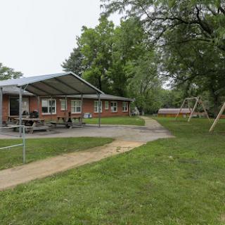 A view of a recreational building surrounded by green grass and trees, with a playground visible in the background.