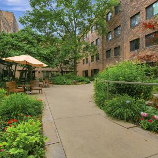 A serene apartment courtyard featuring lush greenery and a shaded seating area.