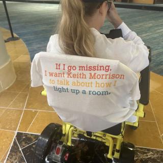 Person in a wheelchair wearing a shirt with printed text.