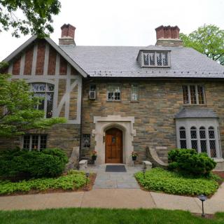 A charming stone Tudor-style house with well-maintained landscaping and prominent chimneys.