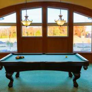 A billiards table in a game room with large windows and chandeliers.
