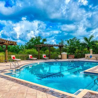 A scenic view of a luxurious swimming pool surrounded by lush greenery and a partly cloudy sky.