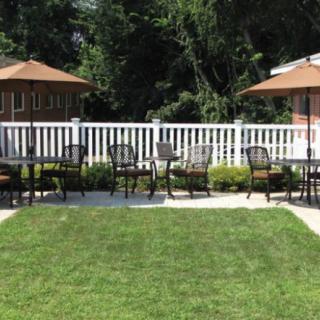 A well-maintained backyard patio area with chairs and umbrellas, bordered by a white fence and lush greenery.