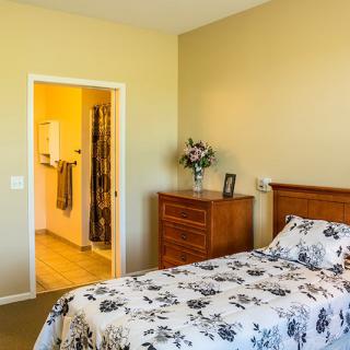A cozy bedroom featuring a bed with floral bedding, a wooden dresser, and an open doorway to a bathroom.