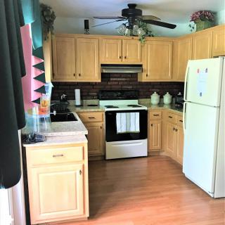 A cozy kitchen with wooden cabinets, a stove, refrigerator, and ceiling fan.
