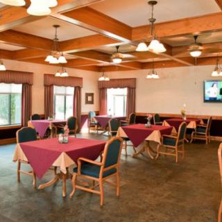 A spacious and well-lit dining area with neatly arranged tables and chairs, featuring large windows and ceiling lights.
