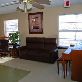 A cozy living room featuring a brown sofa, a piano, and natural light streaming in through the windows.