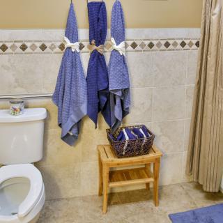 A bathroom with blue towels hanging, a toilet, and a wooden stool holding a basket.