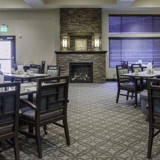 A cozy dining room with multiple tables and chairs, featuring a stone fireplace.