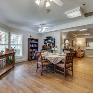 A cozy dining and living area with a wooden table, chairs, bookshelf, and ceiling fan.