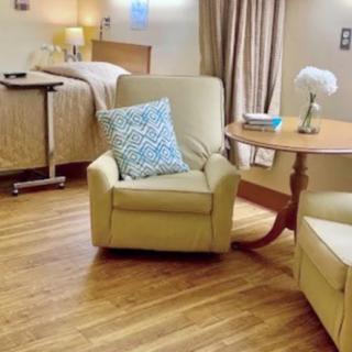 A comfortable hospital room with a bed, armchair, table, and decor.