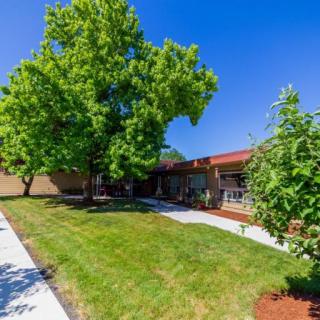 A sunny day with a view of a building surrounded by lush green trees and a well-maintained lawn.