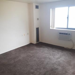 An empty room with carpet flooring, a window, and an air conditioning unit.