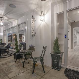 A cozy porch area with chairs, a table, and decorative plants illuminated by soft lighting.