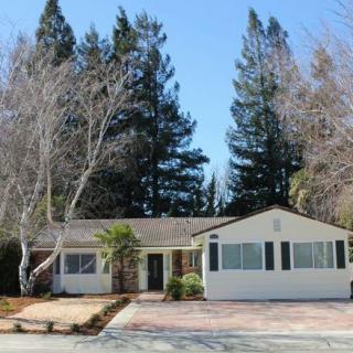 A suburban single-story house with a paved driveway and surrounded by trees.