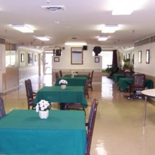 An empty dining area with tables covered in green tablecloths and decorated with flowers.