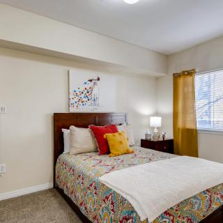 A cozy bedroom with a neatly made bed, colorful pillows, and wall art next to a window with curtains.