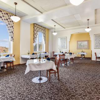An elegant dining room with neatly arranged tables and chairs, featuring large windows and sophisticated decor.