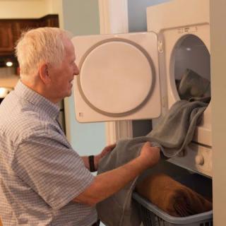 An elderly person doing laundry, loading clothes into a dryer.