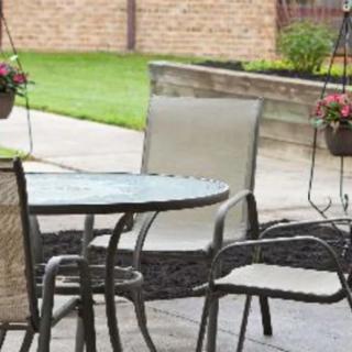 A patio scene featuring outdoor furniture with chairs and a table, surrounded by hanging plants.
