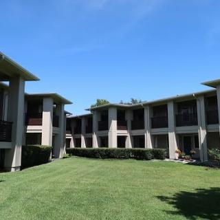 A modern apartment complex with a central grassy courtyard under a clear blue sky.