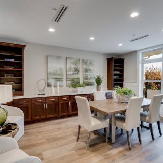 A modern dining room with elegant furnishings, featuring wood floors, built-in bookshelves, and decorative plants.