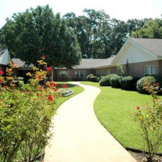 A serene garden walkway lined with vibrant flowers and neatly trimmed hedges leading to a house.