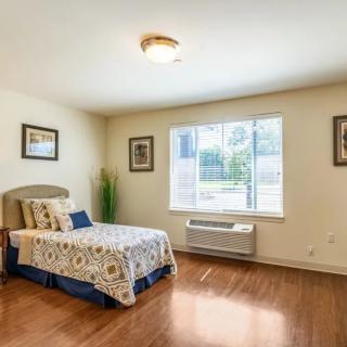 A cozy bedroom with a single bed, hardwood floors, and a large window letting in natural light.