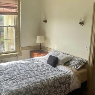 A cozy bedroom with a neatly made bed, a nightstand with a lamp, and a large window.